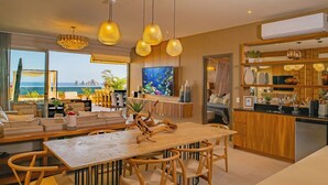 A modern kitchen with wooden countertops, a dining area with a wooden table and chairs, and a large window overlooking the sea.