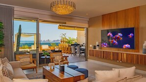 A modern living room with a large TV, comfortable seating, and a view of the sea.