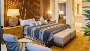 A modern bedroom with a large bed, bedside tables with lamps, a wooden accent wall, and a view into the bathroom.