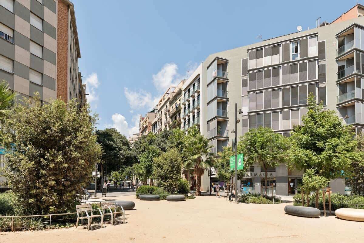 Una plaza urbana moderna con edificios, árboles y bancos.