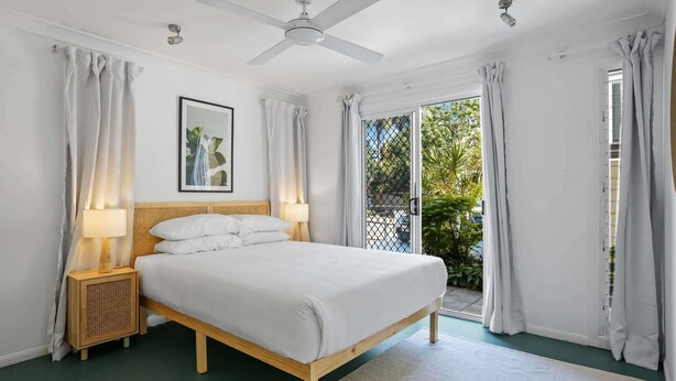 A bedroom with a bed, two bedside tables with lamps, a ceiling fan, a framed picture on the wall, and a view of greenery outside. - Urban Apartment in the Heart of Paddington (Paddington)