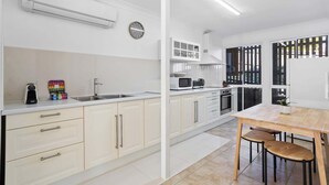 A modern kitchen with white cabinetry, a built-in microwave, and a dining area with a wooden table and chairs. - Urban Apartment in the Heart of Paddington (Paddington)
