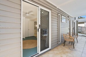 Une terrasse couverte avec une porte-fenêtre coulissante, un ventilateur de plafond et un fauteuil en osier.