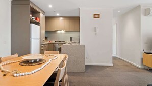 A modern kitchen with a dining area, featuring a granite countertop, stainless steel appliances, and a small island. - Gorgeous 3-Bed Apartment Near Flagstaff Gardens (West Melbourne)