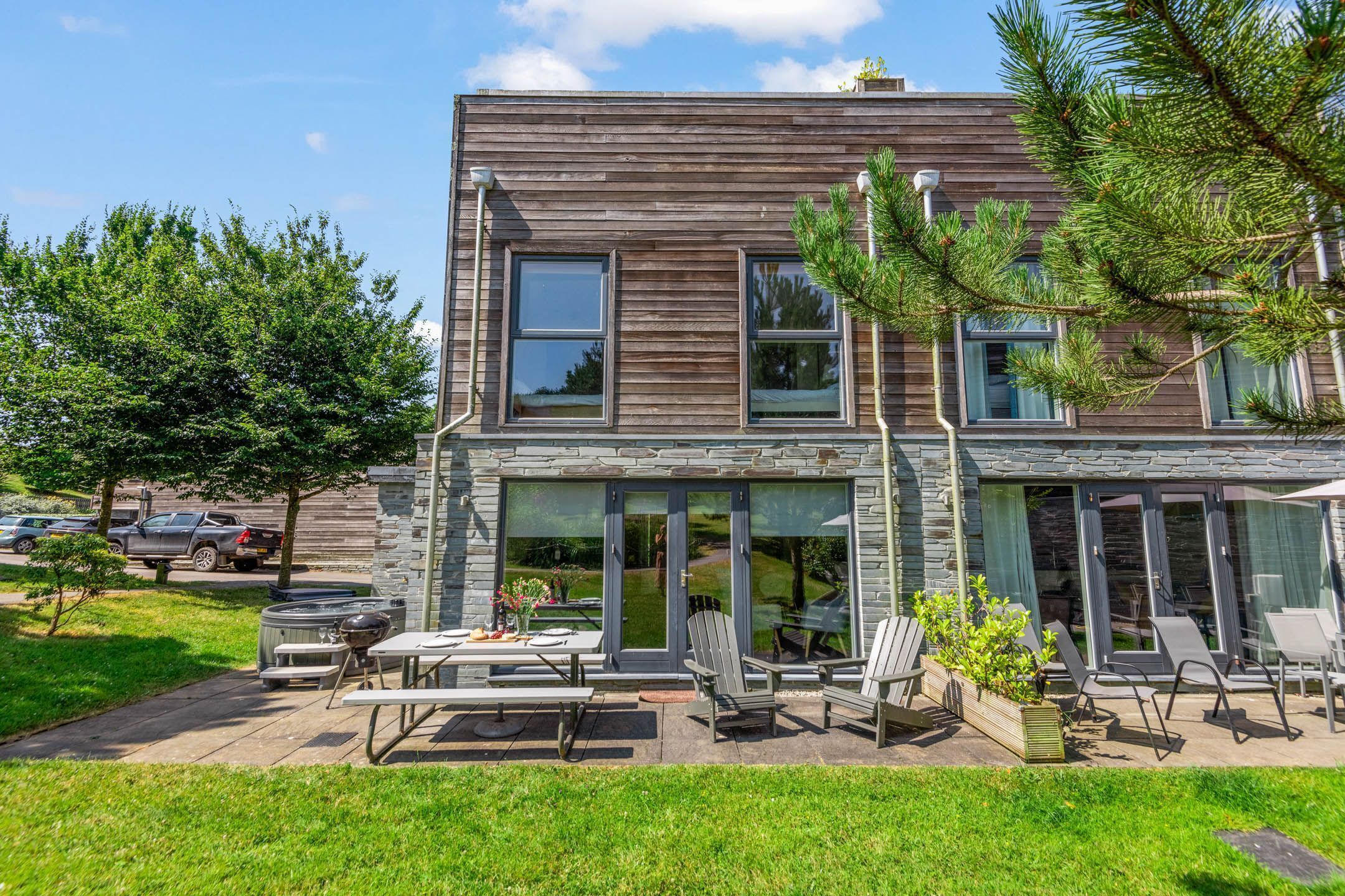 A modern two-story building with a stone facade, large windows, and an outdoor patio with seating and a grill.