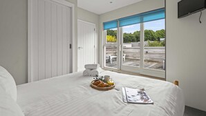 A bedroom with a large bed, a window with a view of the outdoors, and a flat-screen TV mounted on the wall.