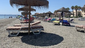 Une plage avec des parasols en chaume et des chaises longues.