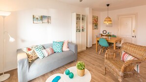 Un salon moderne avec un canapé gris, un fauteuil en osier et un coin repas comprenant une table et des chaises.