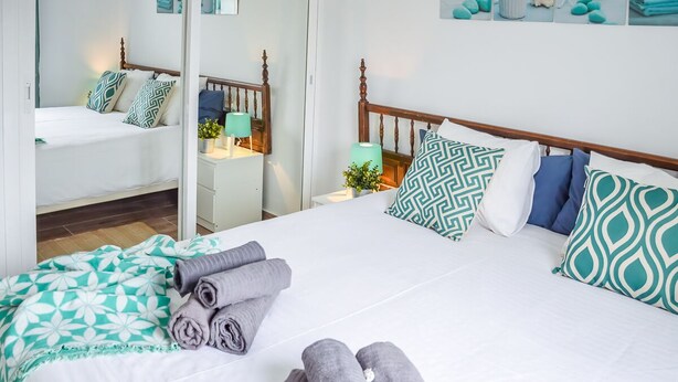 Une chambre bien éclairée, avec un grand lit, deux tables de chevet et un miroir.