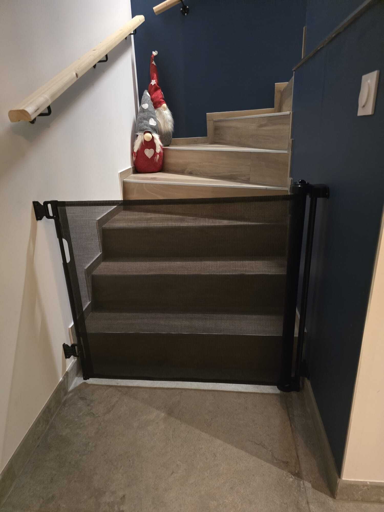 Een trap met een gaas veiligheidshek, een rode gnom decoratie, en een houten leuning.