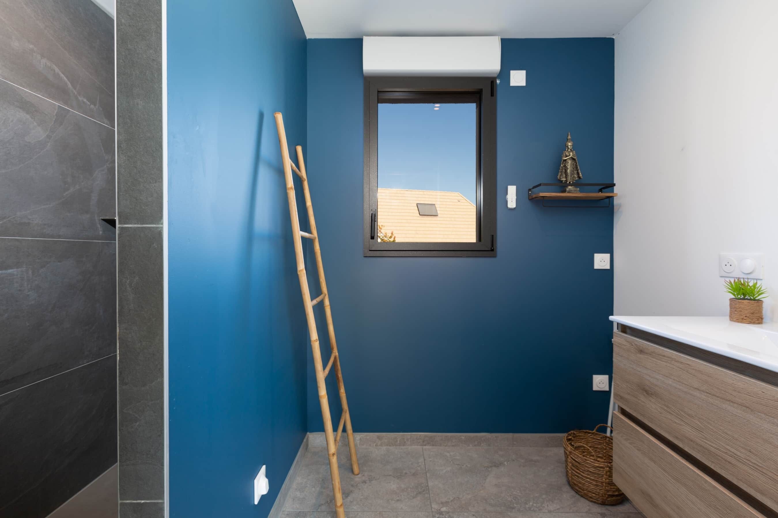 Een badkamer met donkerblauwe wanden, een houten ladder, een raam, een plank met een plant en een houten kast.