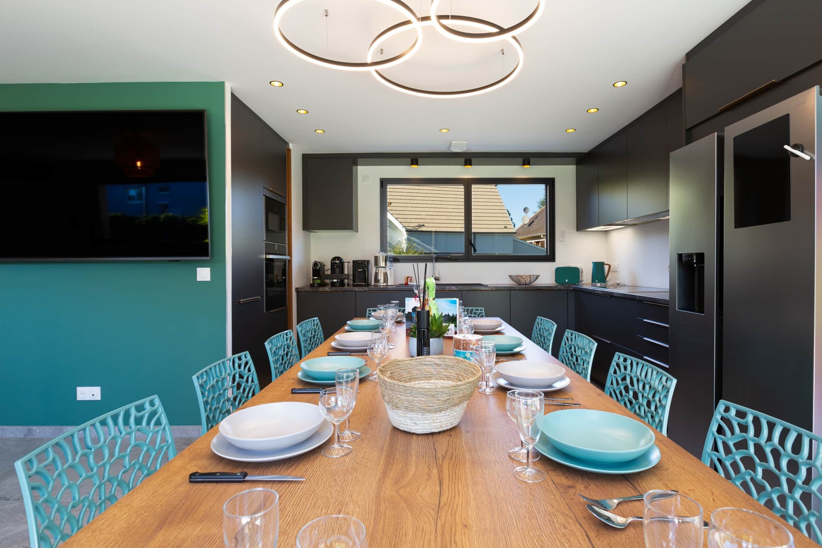 Een moderne eetruimte met een lange tafel voor zes personen, omringd door teal stoelen.