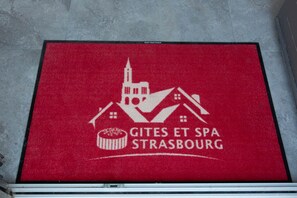 A red mat with a white logo and text reading "Gites et Spa Strasbourg". - Villa Lion | Private Spa, Pool/Jacuzzi, Terrace, Arcade (Ittenheim)