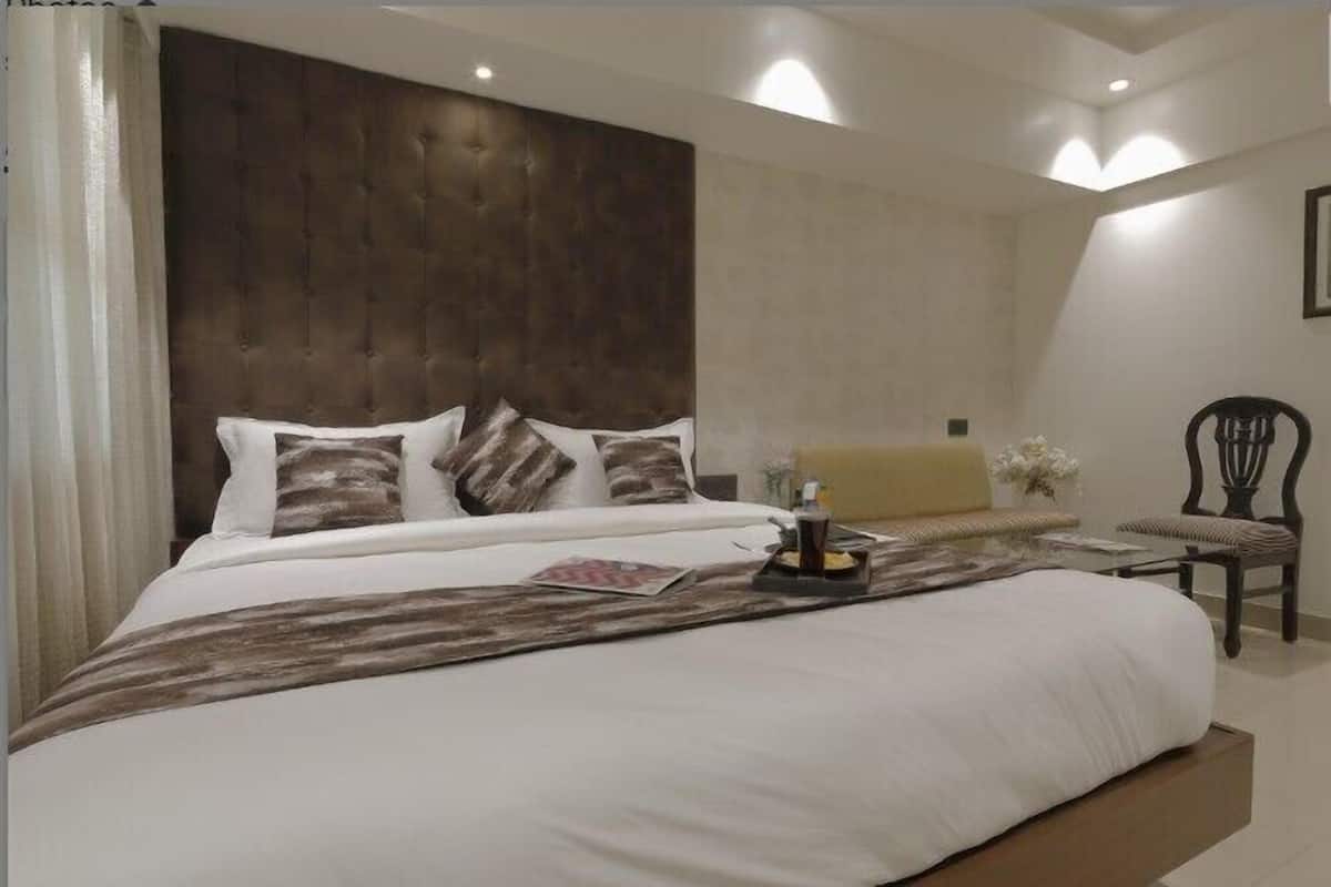 Un dormitorio con una cama grande, cabecera de madera, una mesita de noche con lámpara y una silla.