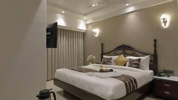 Ein modernes Hotelzimmer mit einem großen Bett, einem Nachttisch mit Lampe, einem an der Wand montierten Fernseher und einer Kaffeemaschine auf dem Boden.
