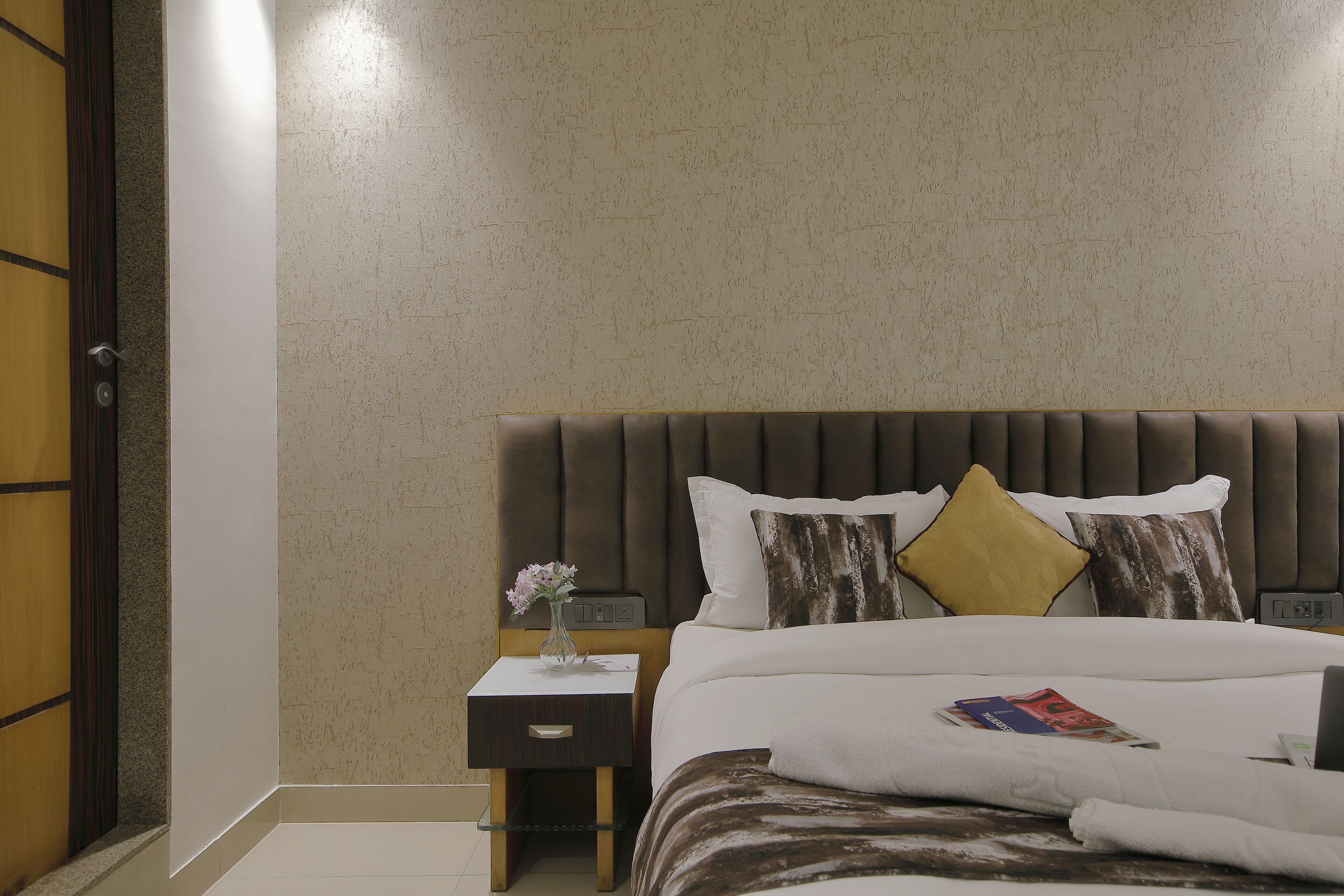 A neatly arranged hotel room with a large bed, a bedside table with a vase, and a modern headboard.