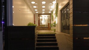 La entrada del Hotel Ariana Residency, con un cartel en varios idiomas, una escalera que conduce a la entrada y un interior bien iluminado.