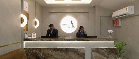A hotel reception desk with marble countertops, a plush sofa, and a reception area with a circular logo.