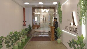 Zona de recepción de hotel con un letrero de bienvenida, una recepcionista y plantas en macetas.