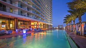 Ein mehrstöckiges Hotel mit Schwimmbad, Außenbereich und Palmen.