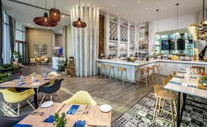 Un hall d’hôtel moderne doté d’un bar, de différents espaces de détente et d’une grande fenêtre.