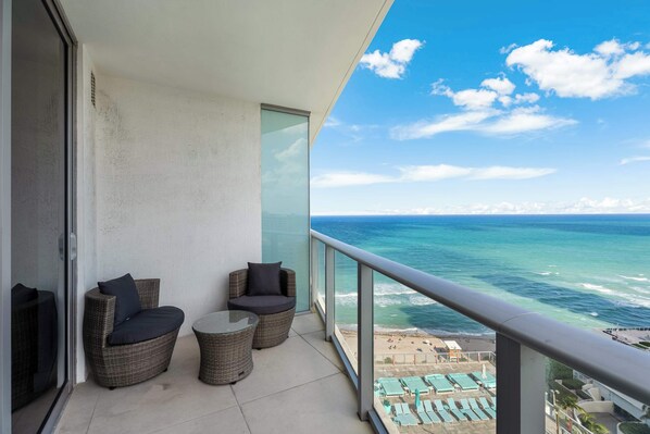 A balcony with wicker furniture, a glass door, and a view of the ocean.