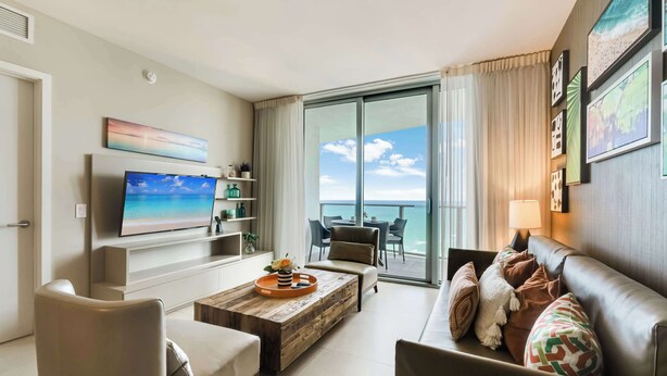Ein modernes Wohnzimmer mit Flachbildfernseher, Couch, Holz-Couchtisch und einem Balkon mit Aussicht.