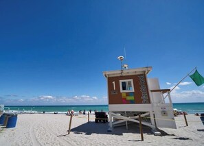 A lifeguard tower with a flag, located on a sandy beach with the ocean in the background.