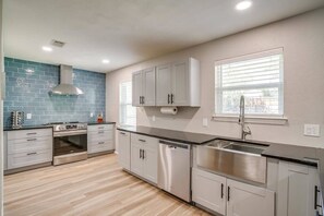 A modern kitchen with grey cabinets, a stainless steel sink, and a blue backsplash.