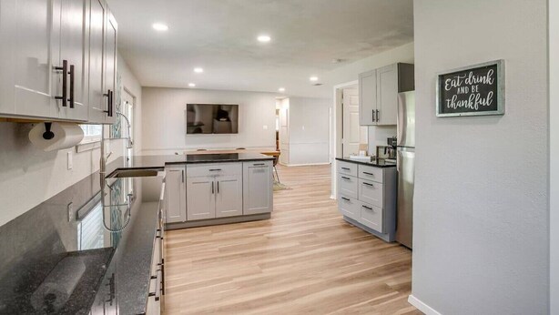Una cocina moderna con una isla central, armarios grises y un refrigerador de acero inoxidable.