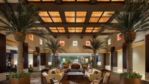 A spacious lobby with a high ceiling, palm trees, comfortable seating, and a view of the outdoors. - Why Wait? Reserve your Villa today! (Phoenix)