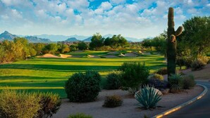 A golf course with a cactus in the foreground, surrounded by desert vegetation and mountains in the background. - Why Wait? Reserve your Villa today! (Phoenix)