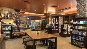 A modern cafe with a wooden table, stools, and shelves stocked with snacks and beverages. - Why Wait? Reserve your Villa today! (Phoenix)