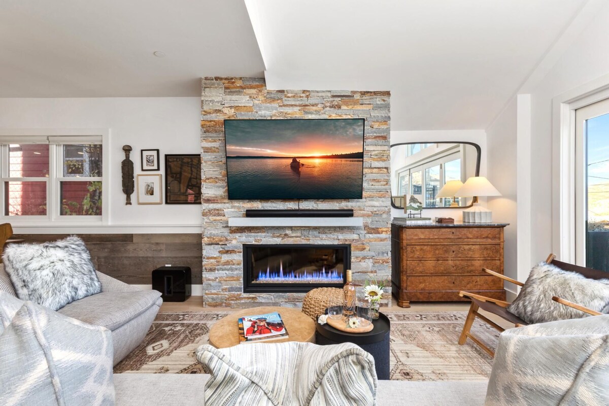 A modern living room with a stone fireplace, a large flat-screen TV mounted above it, and a cozy seating area with two sofas and a coffee table.
