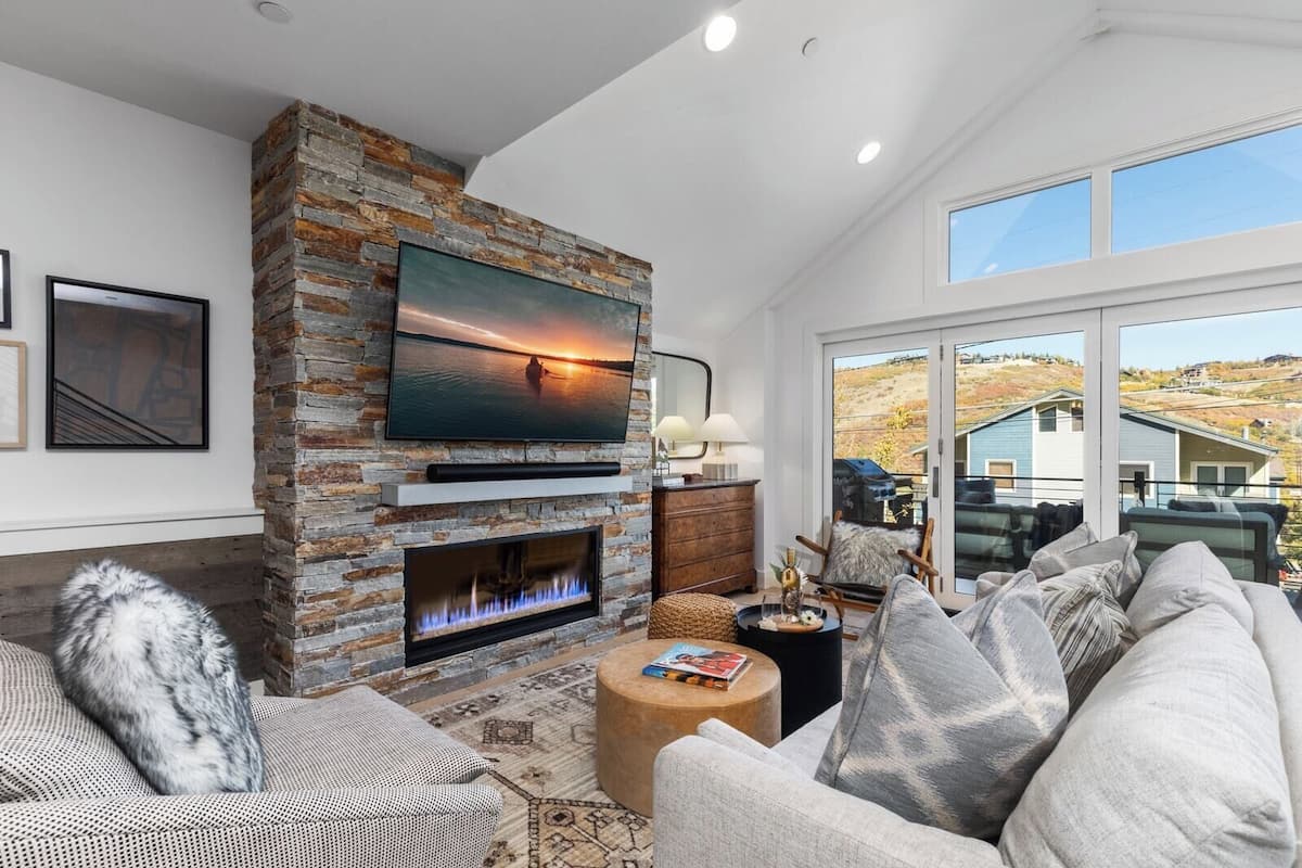 A modern living room with a stone fireplace, a flat-screen TV, and a large window overlooking a scenic landscape.