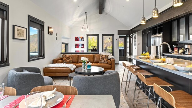 A modern kitchen with a bar area, a dining table with chairs, and a living area with a sofa and armchairs.