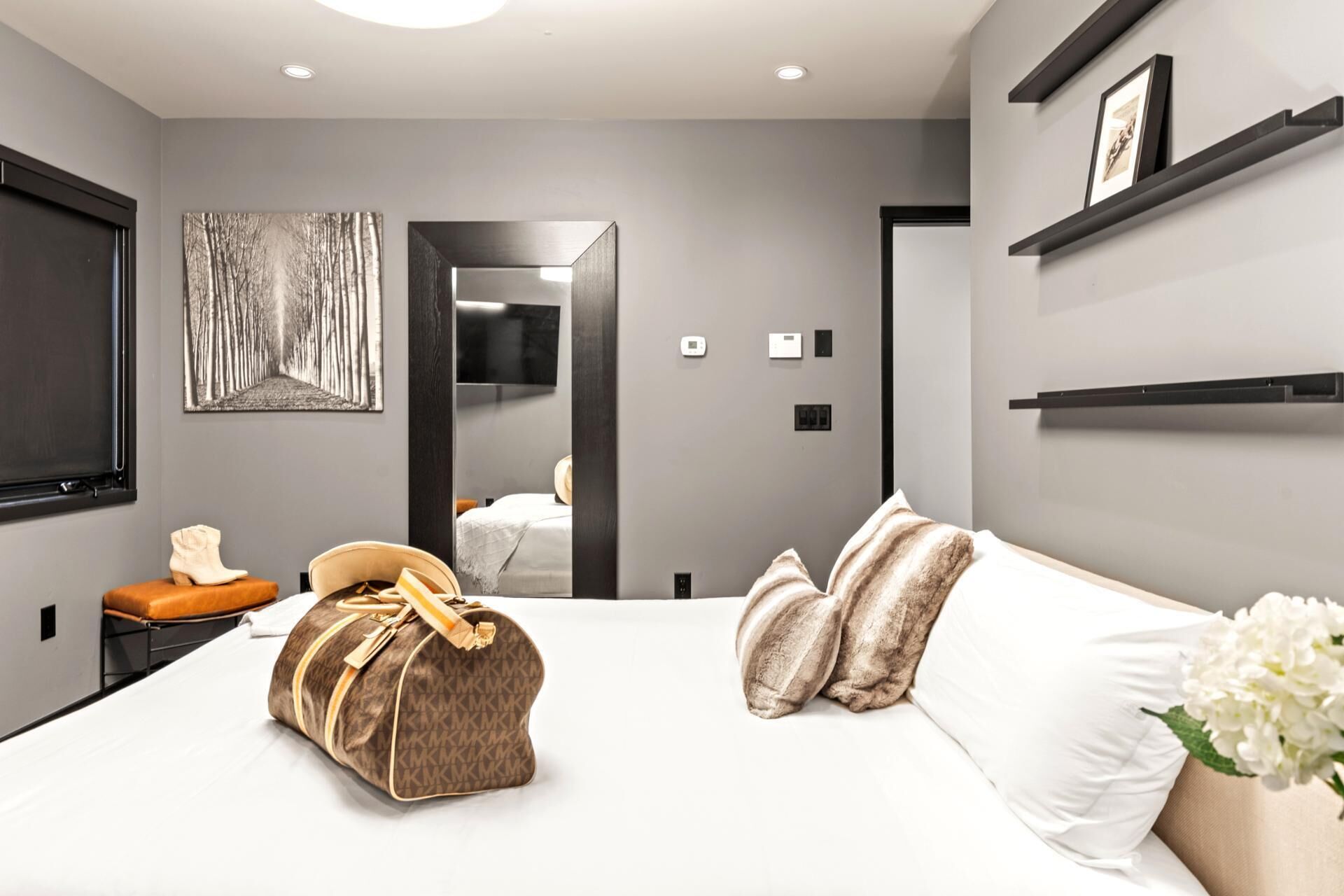 A modern hotel room with a large bed, a bedside table, a mirror, and a wardrobe.