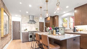 A modern kitchen with a central island, bar stools, pendant lighting, and wooden cabinetry.