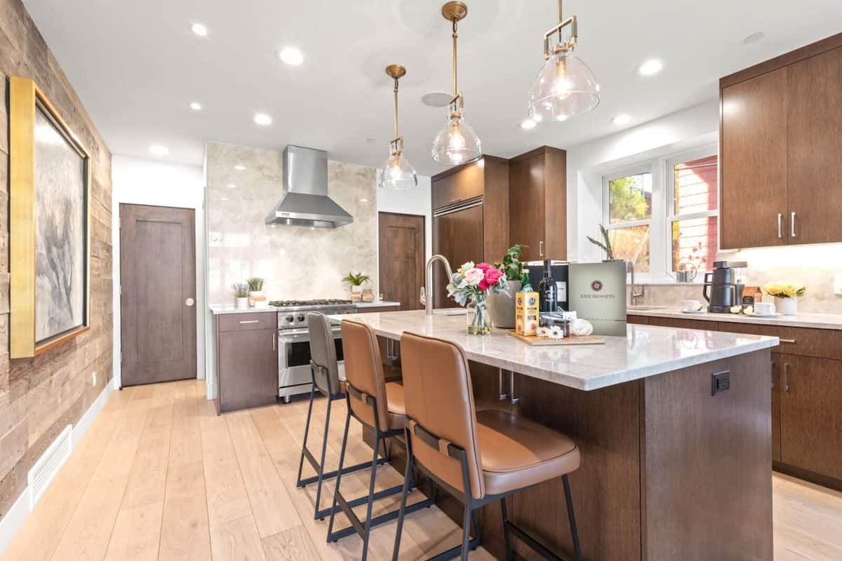 A modern kitchen with a central island, bar stools, pendant lighting, and wooden cabinetry.