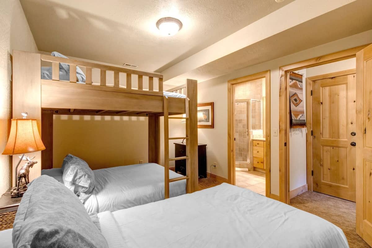 A room with two beds, a bunk bed, a lamp, and a door leading to another room.
