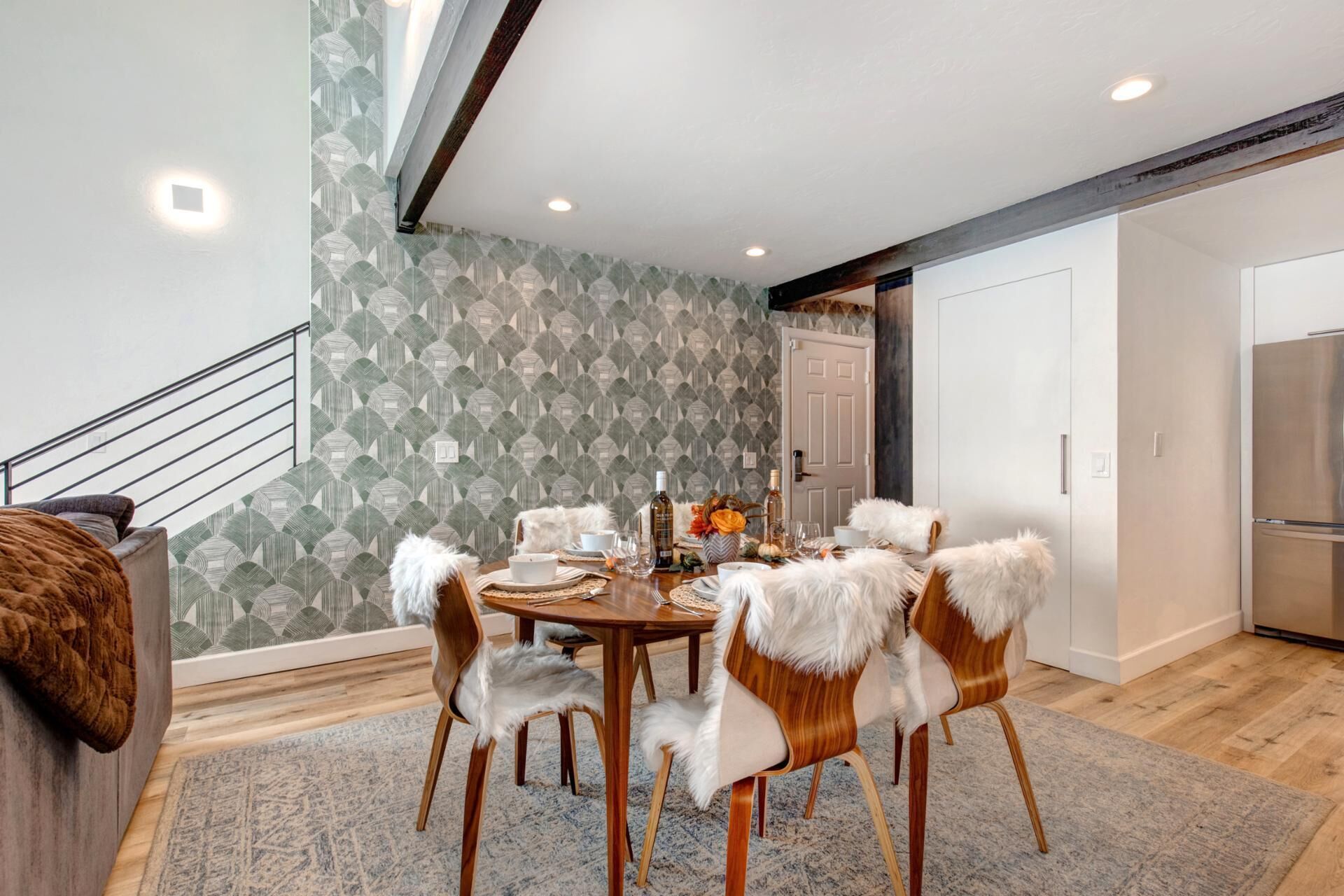 A dining area with a round table, six chairs with white fur trim, and a patterned wallpaper.