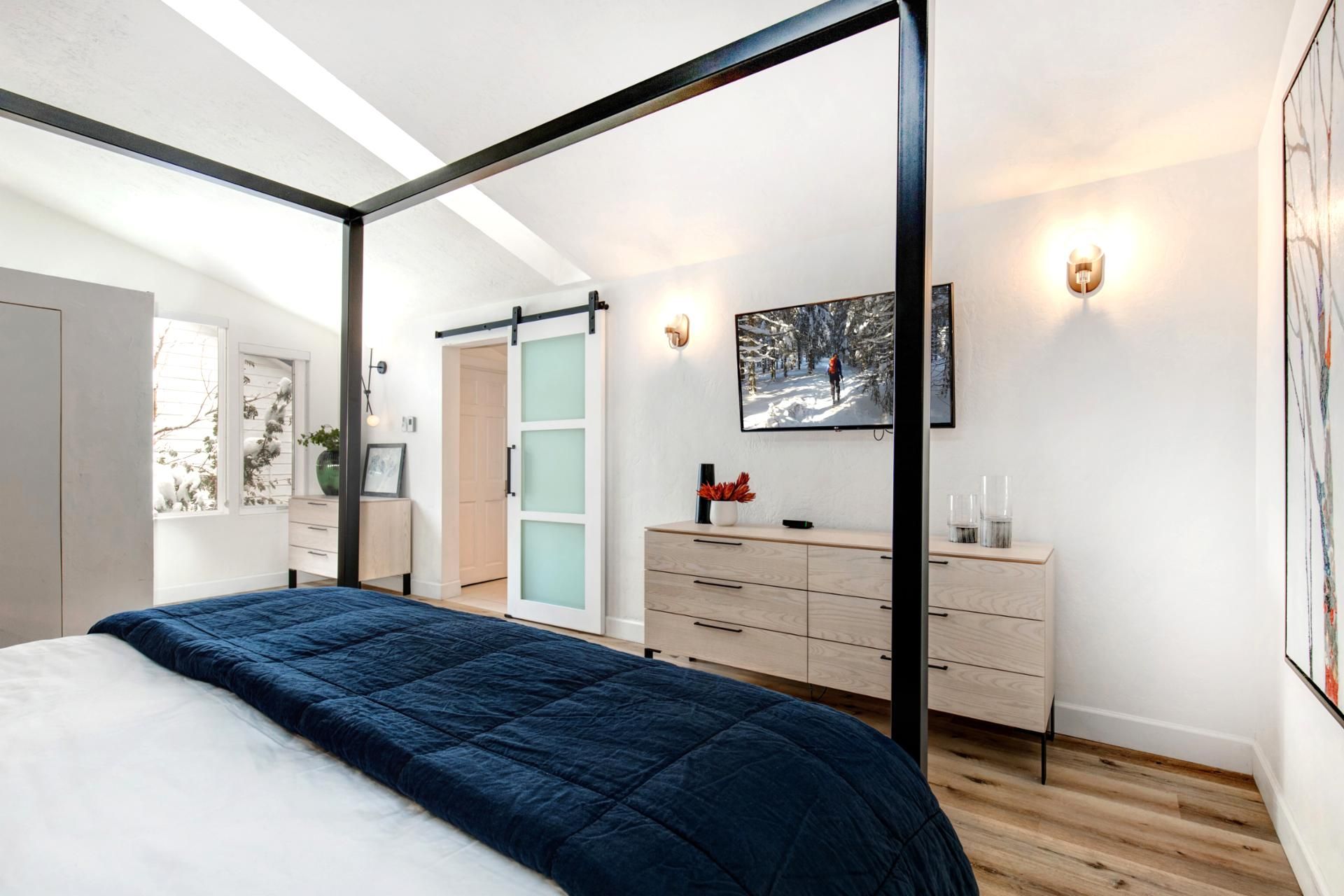 Ein modernes Schlafzimmer mit einem Himmelbett, einer Schiebetür, einer hölzernen Kommode und einem gerahmten Bild an der Wand.
