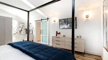 Ein modernes Schlafzimmer mit einem Himmelbett, einer Schiebetür, einer hölzernen Kommode und einem gerahmten Bild an der Wand.