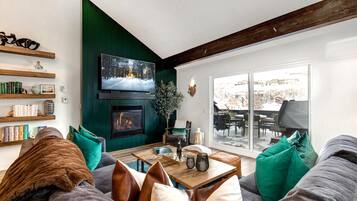 A cozy living room with a fireplace, bookshelves, and a large window offering a view of the outdoors.