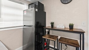 A compact kitchen with a refrigerator, a microwave, a clock, and a small table with two stools. - Stylish Queen Suite : Near Beach + Shops + Dining (Fort Lauderdale)