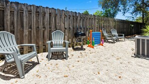 A backyard with a wooden fence, outdoor seating with chairs, a barbecue grill, and a portable air conditioning unit. - Stylish Queen Suite : Near Beach + Shops + Dining (Fort Lauderdale)