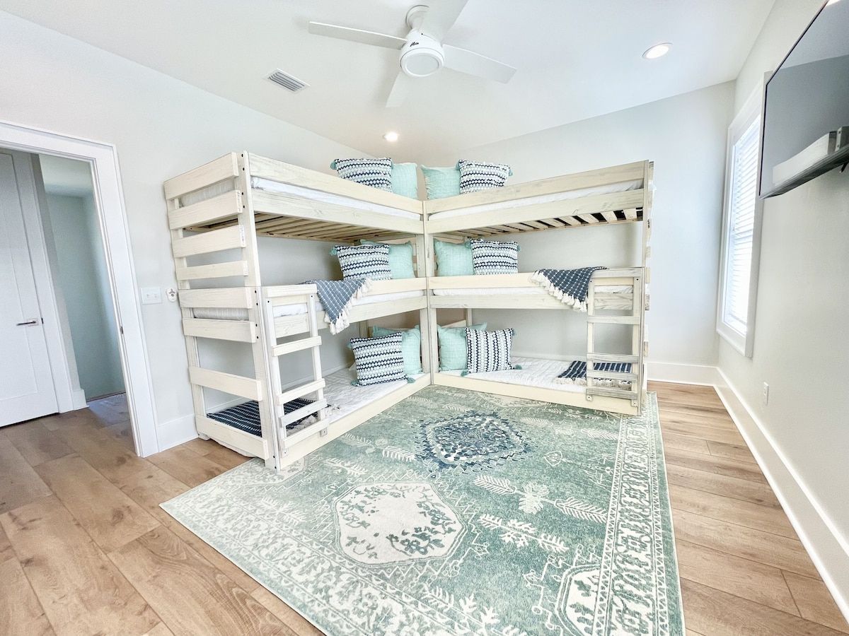 Ein Eckzimmer mit Etagenbett, einem gemusterten Teppich und einem Deckenventilator.