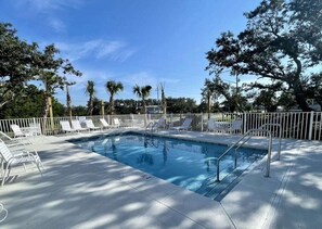 Relax by the pool surrounded by lush trees and comfortable lounge chairs.