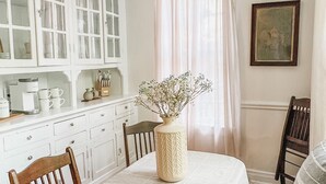 A dining area with a table set for four, surrounded by wooden chairs. A vase with flowers is placed on the table. - Historic Midtown Chateau + Guest House - Minutes from Everything (Memphis)