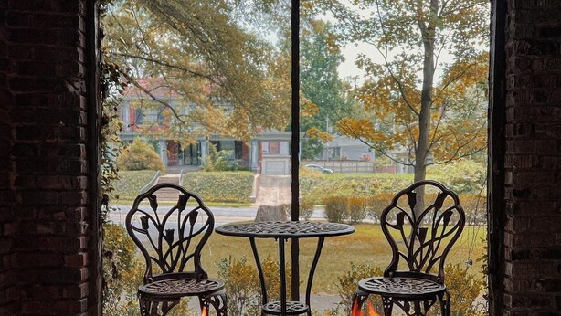 A fire pit with flames, two chairs, and a table in a brick-walled room with a view of a residential area. - Historic Midtown Chateau + Guest House - Minutes from Everything (Memphis)